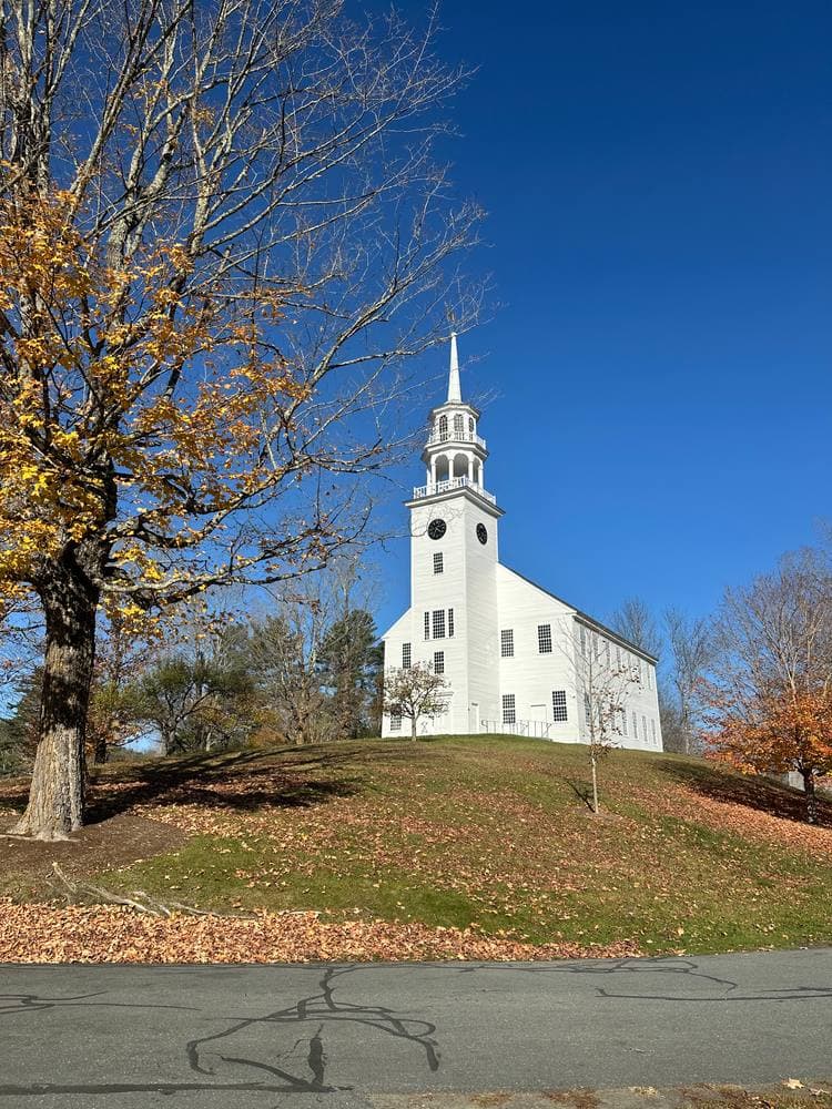 The historic white Town House of Strafford, Vermont, steeple against a deep blue sky on its leafy hill