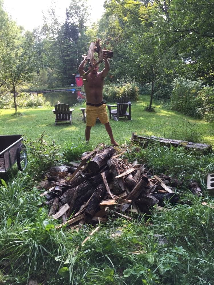 Splitting firewood barefoot beside the pond, Adirondack chairs and the red shed behind