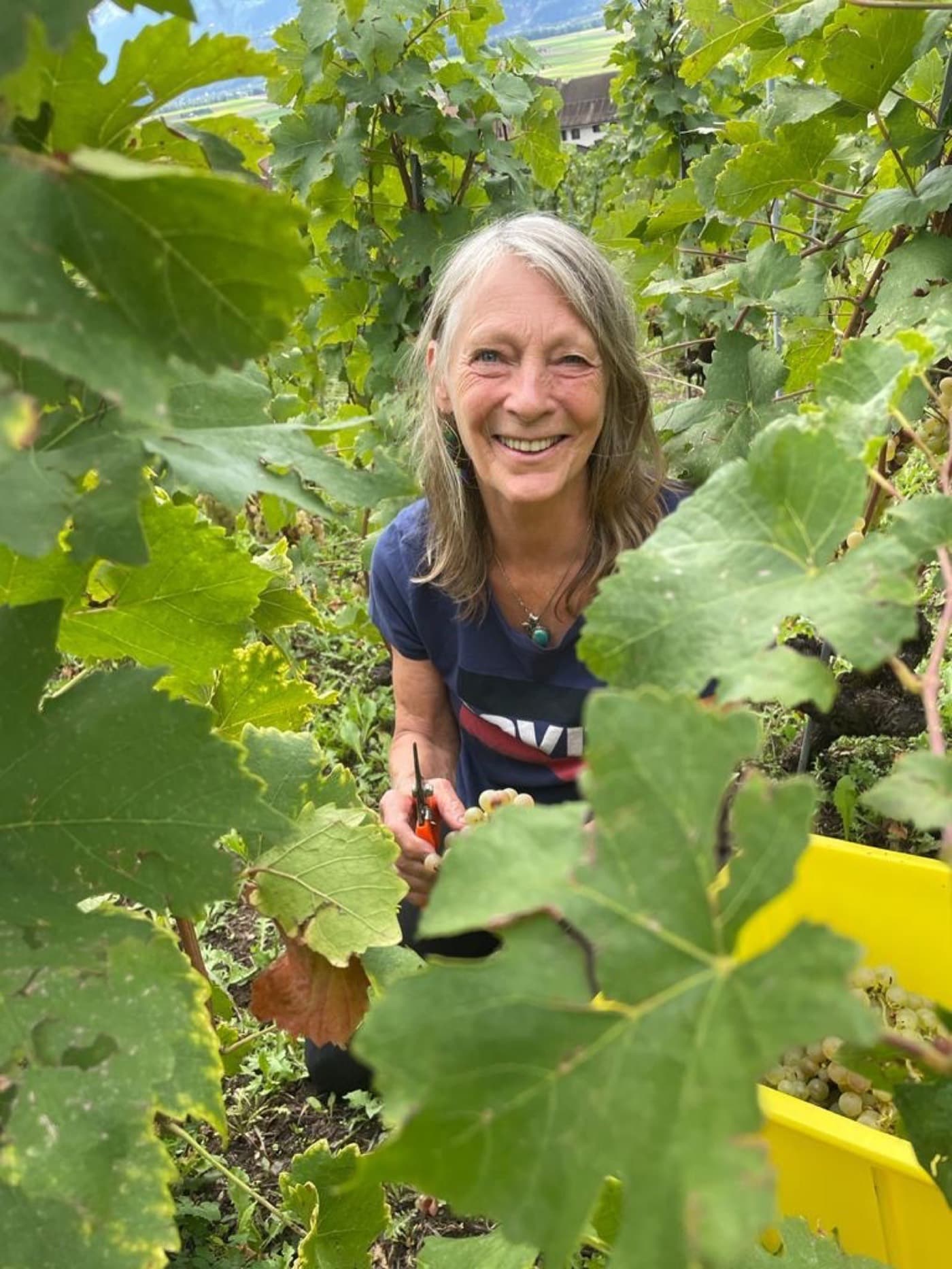 Aletta smiling among tall green vines and leaves in her garden